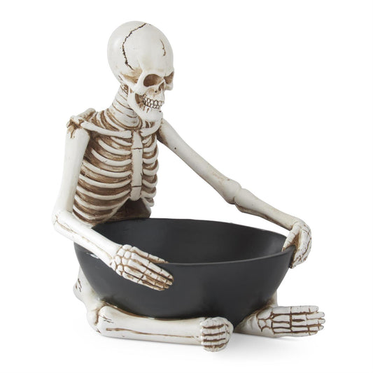 A Halloween skeleton figurine sitting cross-legged and holding a black bowl, photographed against a solid white background.