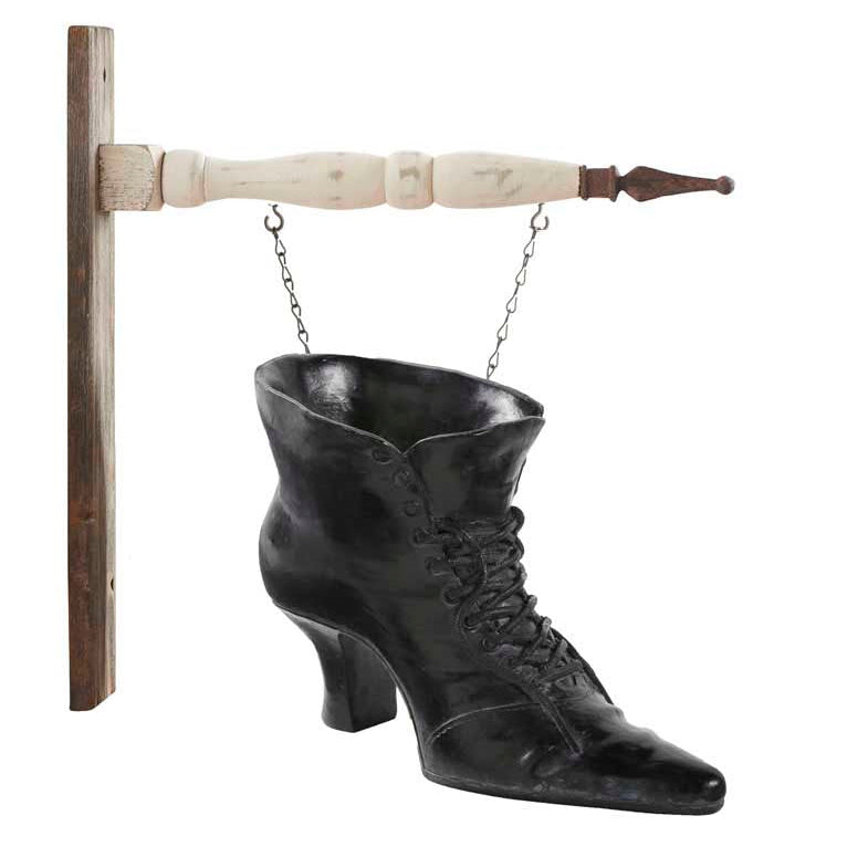 A black resin arrow replacement sign designed to look like a witch's boot, intended to be hung on an arrow bracket, with a white and brown wooden bracket visible in the background.