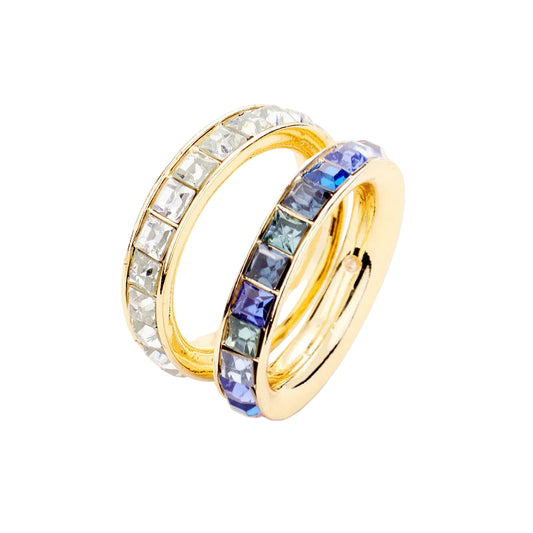 A set of two square eternity gemstone band rings, one with blue gemstones and the other with clear gemstones, both set in gold-colored metal.