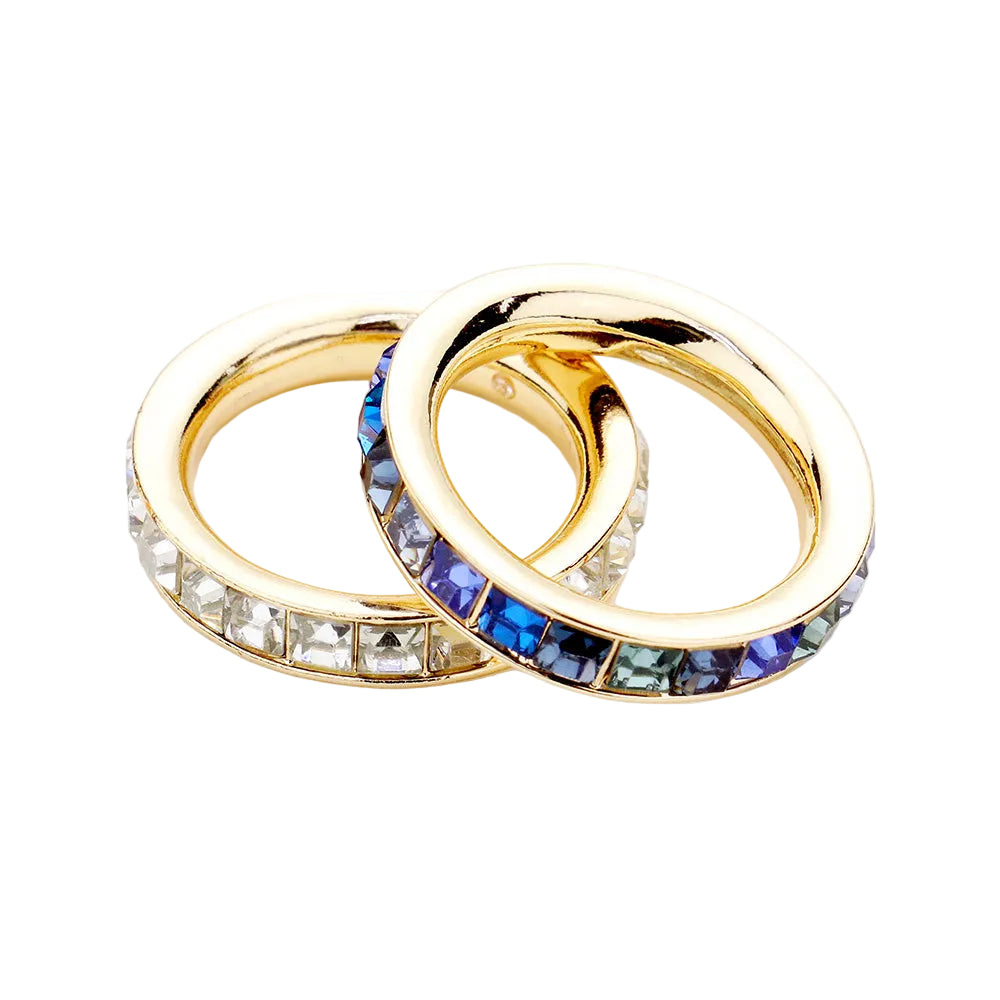A set of two eternity band rings with blue and clear gemstones with gold-colored bands.