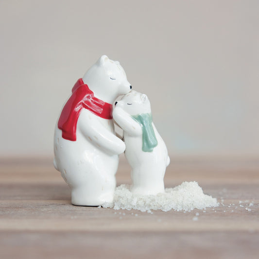 Two white polar bear salt and pepper shakers hugging with scarves on a wooden surface.