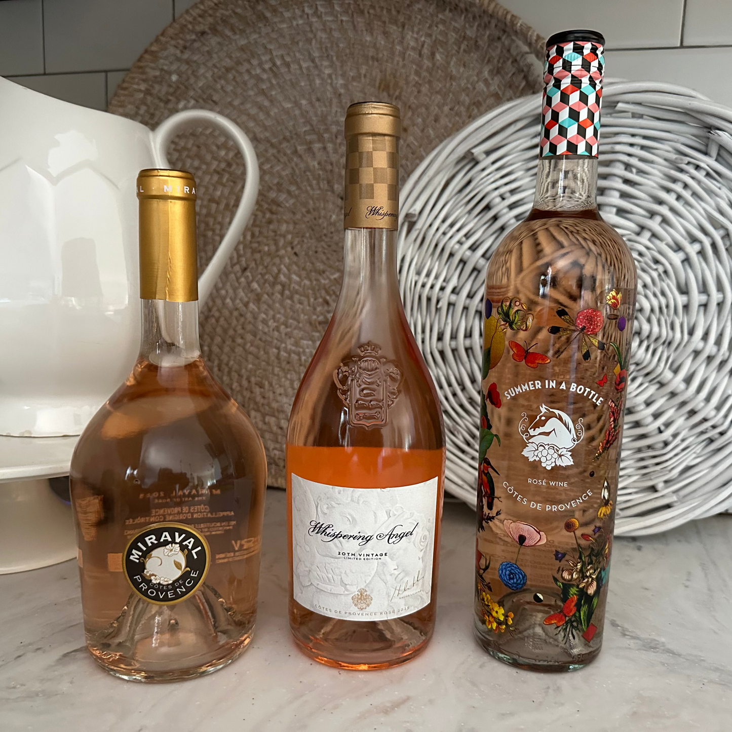 Three bottles of wine on a kitchen counter with decorative plates in the background.