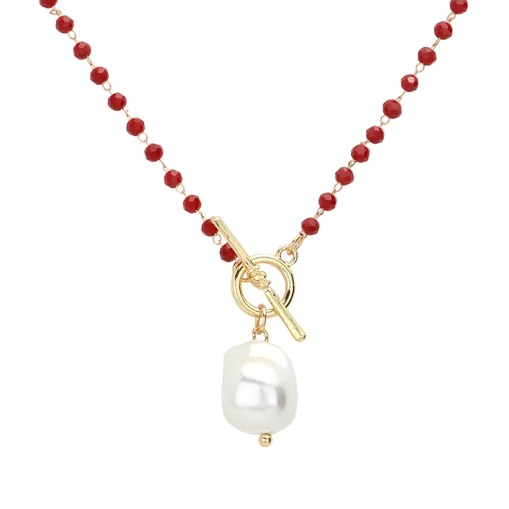 A gold-colored toggle necklace with faceted burgundy beads and a pearl pendant