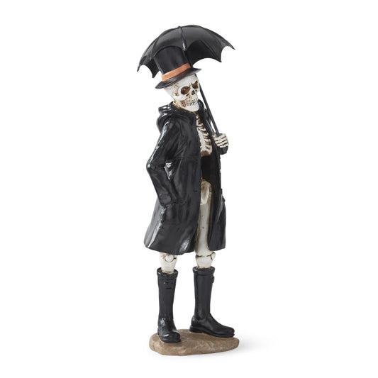A skeleton figurine dressed in a black raincoat, black boots, and holding a black umbrella, standing on a small brown base against a white background.