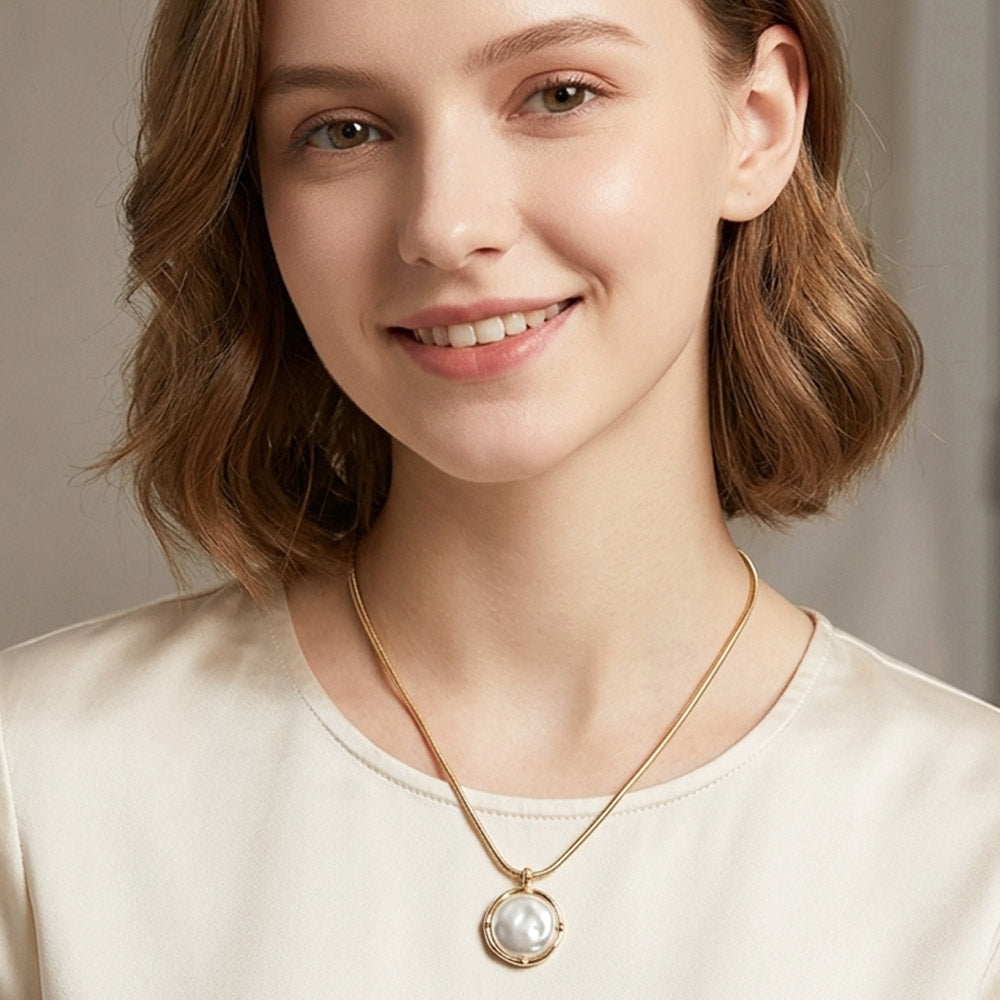 Woman wearing a gold necklace with a pearl pendant against a neutral background