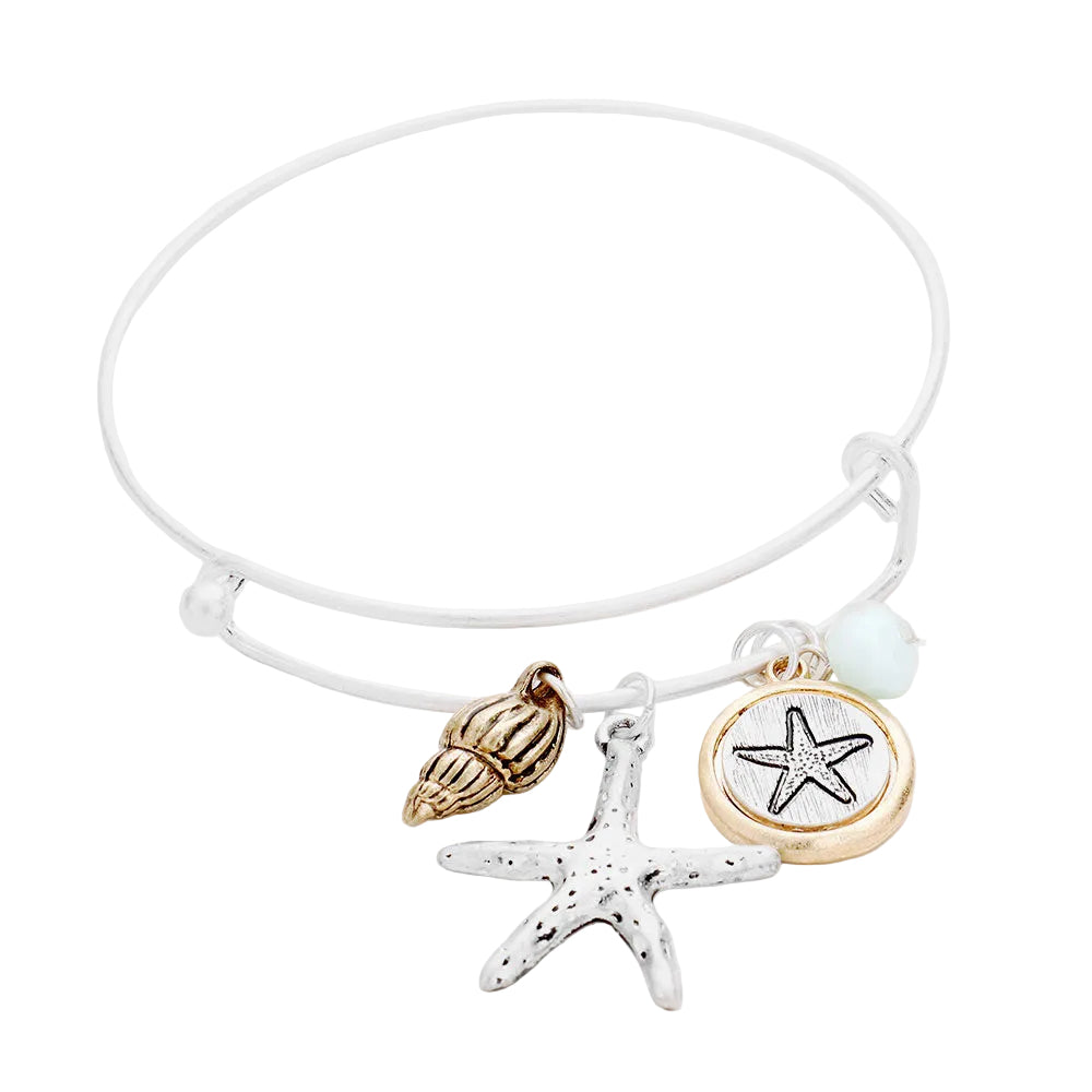 A bracelet with a cream-colored band and charms including a starfish and a shell in gold and silver tones.