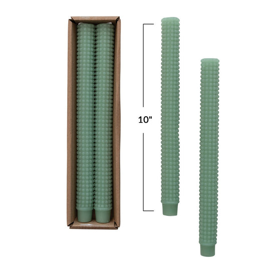 Green hobnail textured taper candles with packaging on a white background