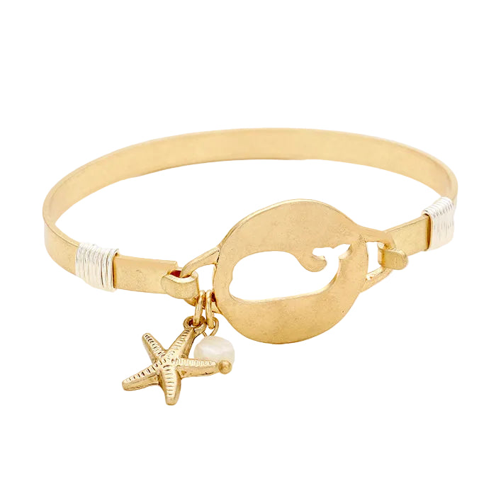 A gold-tone bracelet featuring a cut out whale design with a starfish charm attached to it.