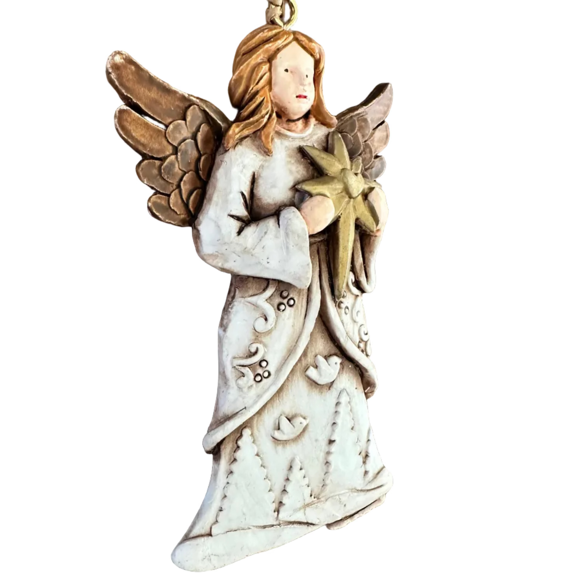 A handcrafted angel Christmas ornament hanging on a rustic dark wood surface. The ornament depicts an angel with reddish-brown hair, brown wings, and a weathered off-white robe holding a gold star.