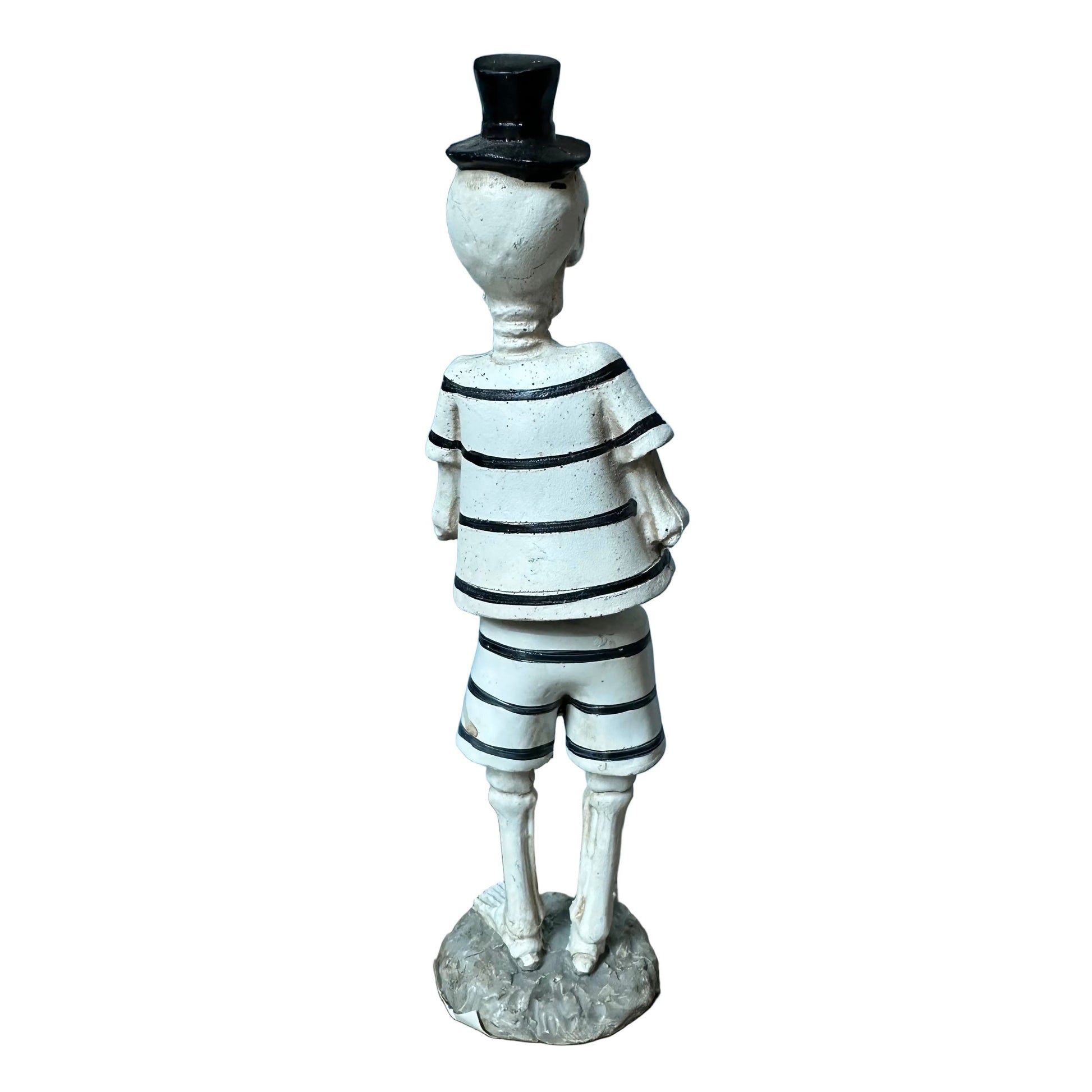 A small figurine of a skeleton wearing a black-and-white striped shirt and shorts, a black top hat, and standing on a round base against a plain white background.