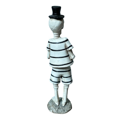 A small figurine of a skeleton wearing a black-and-white striped shirt and shorts, a black top hat, and standing on a round base against a plain white background.