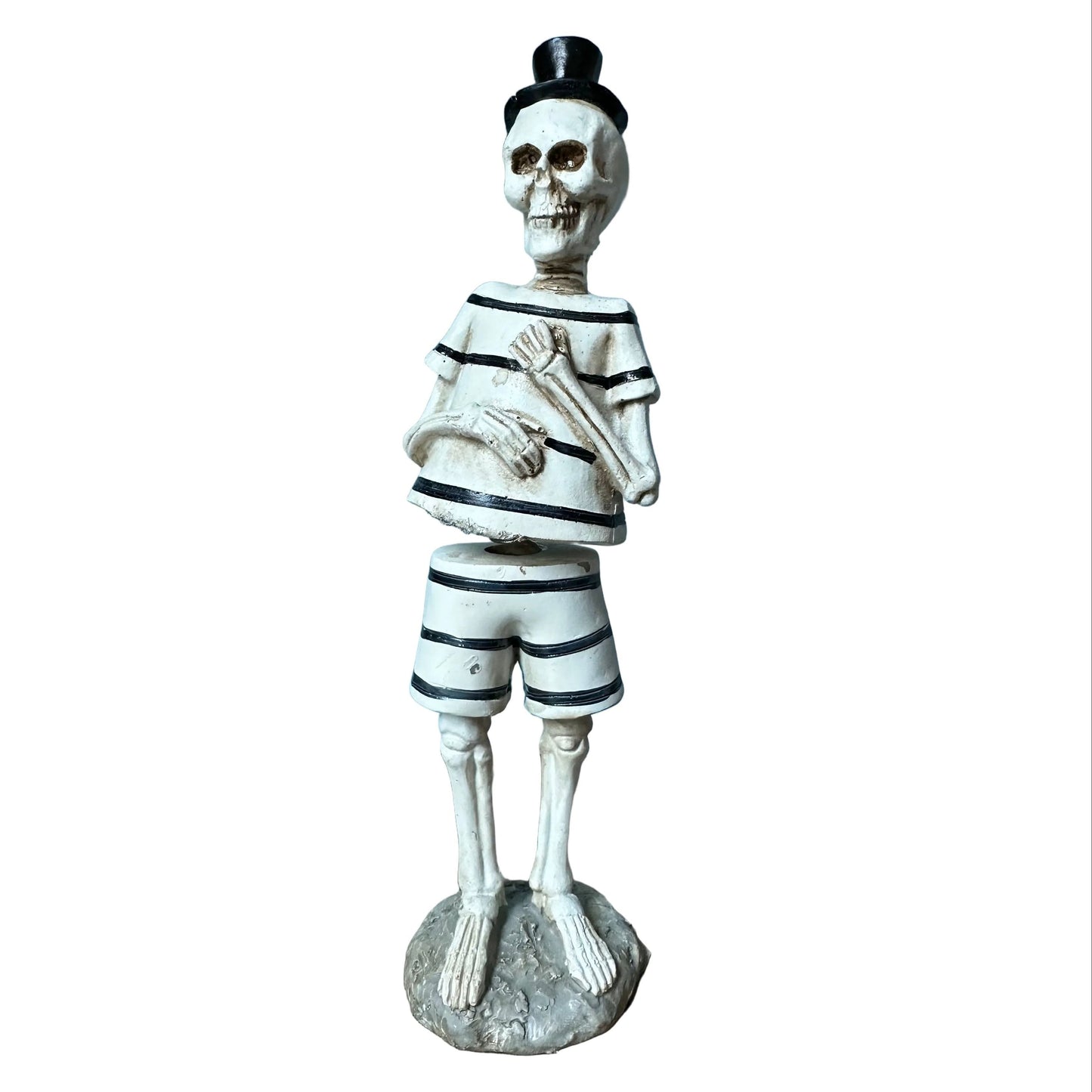 A decorative skeleton figurine dressed in a black-and-white striped sailor shirt and shorts, wearing a small black top hat and standing on a round base against a plain white background.