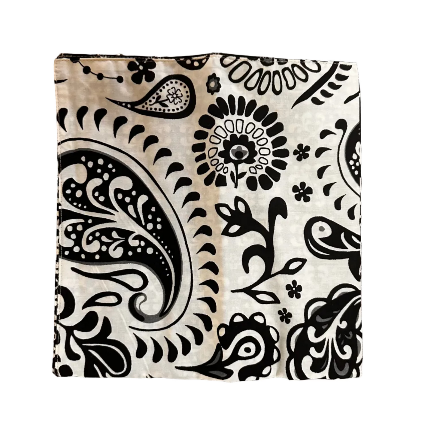 A square fabric item, a napkin, featuring a black paisley and floral block print on a cream-colored background, laid flat on a white surface
