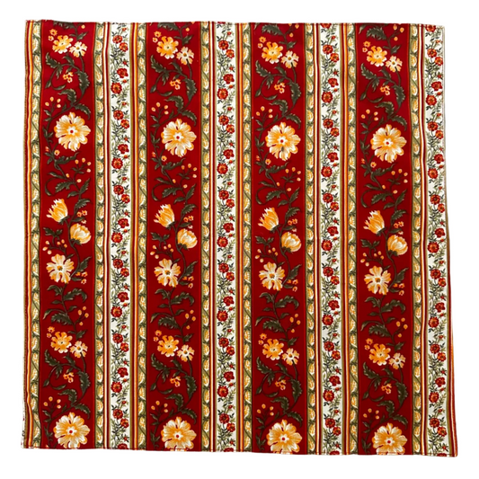 A square napkin with a vertical floral pattern in red, cream, orange, and green, laid flat on a white background.