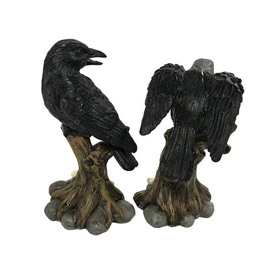 A pair of black raven figurines perched on weathered tree trunks with gray stone-like bases, shown against a plain white background.
