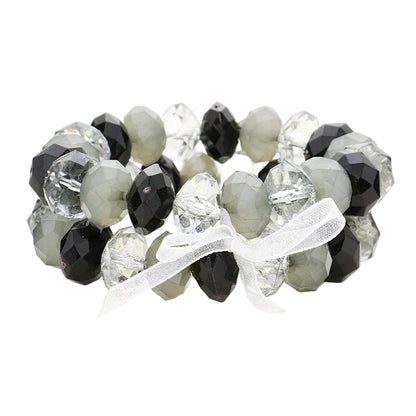 A two-piece stretchable bracelet set featuring faceted lucite beads in black and clear colors, with a white ribbon bow detail.
