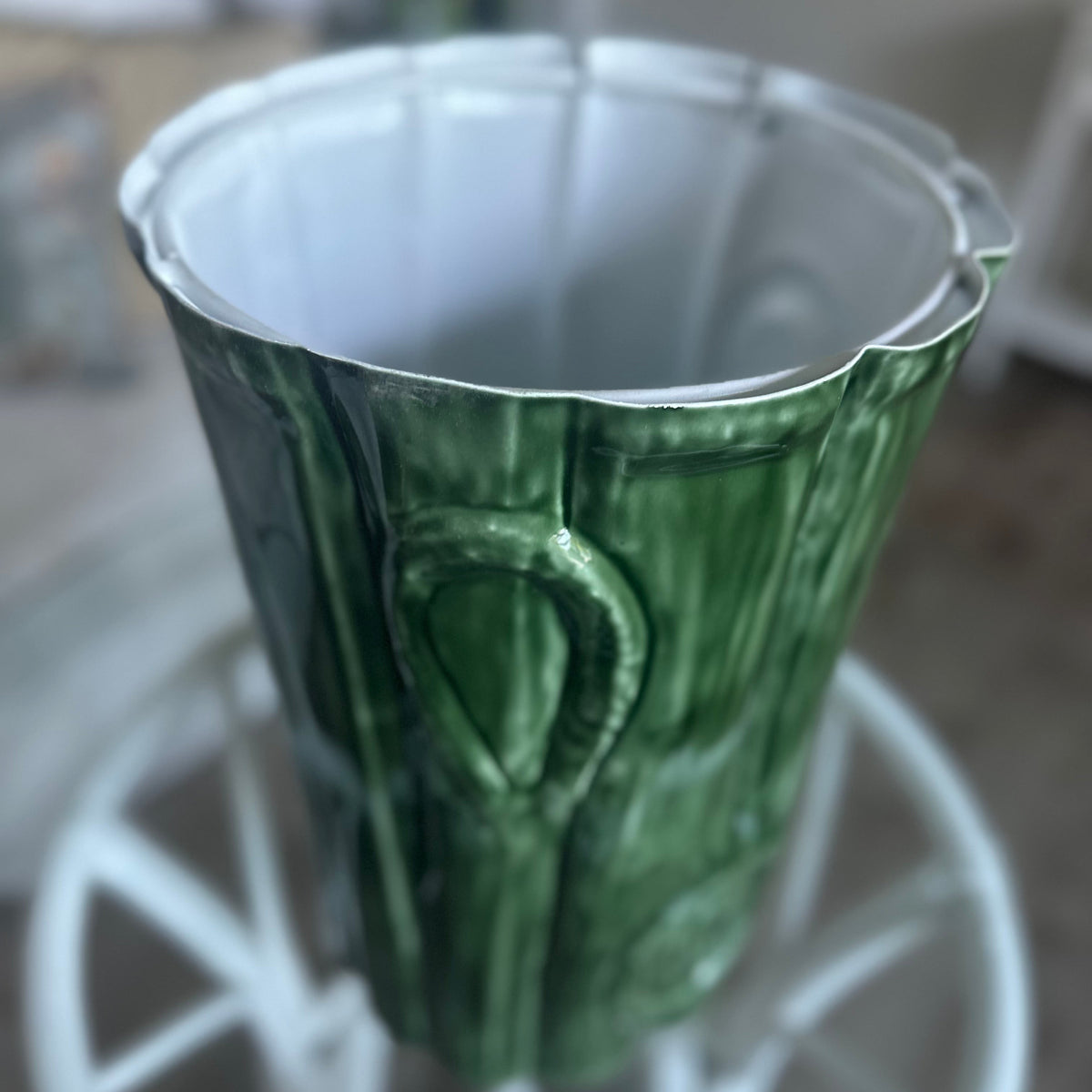 A green metal planter shaped like a tree trunk with a ribbed, textured surface and a flared rim, displayed on a white wire stand.
