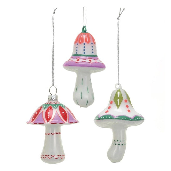Three hand-painted glass Christmas mushroom ornaments in pink, red, green, and purple colors, hanging from silver strings against a white background.