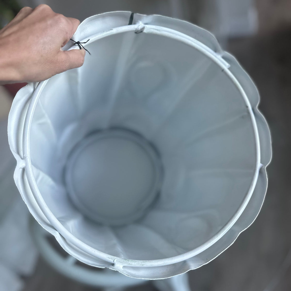 A close-up view from above of the interior of the green metal tree trunk stool which is white being held by a hand, with a blurred indoor room in the background.