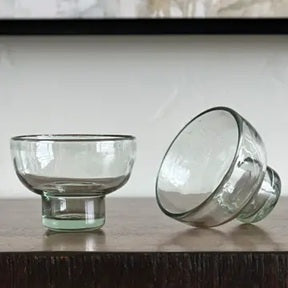 Two clear glass margarita glasses -bowls on a wooden surface with a neutral background