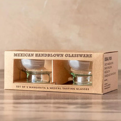 Set of 2 Mexican handblown glassware tasting glasses in a cardboard box on a wooden surface.