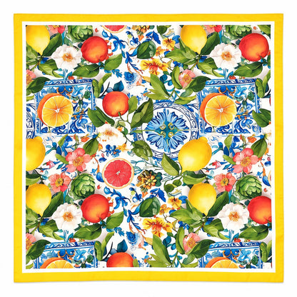 A square scarf featuring a vibrant Mediterranean-style print with lemons, oranges, grapes, flowers, and blue-and-white tiles, framed by a solid yellow border.