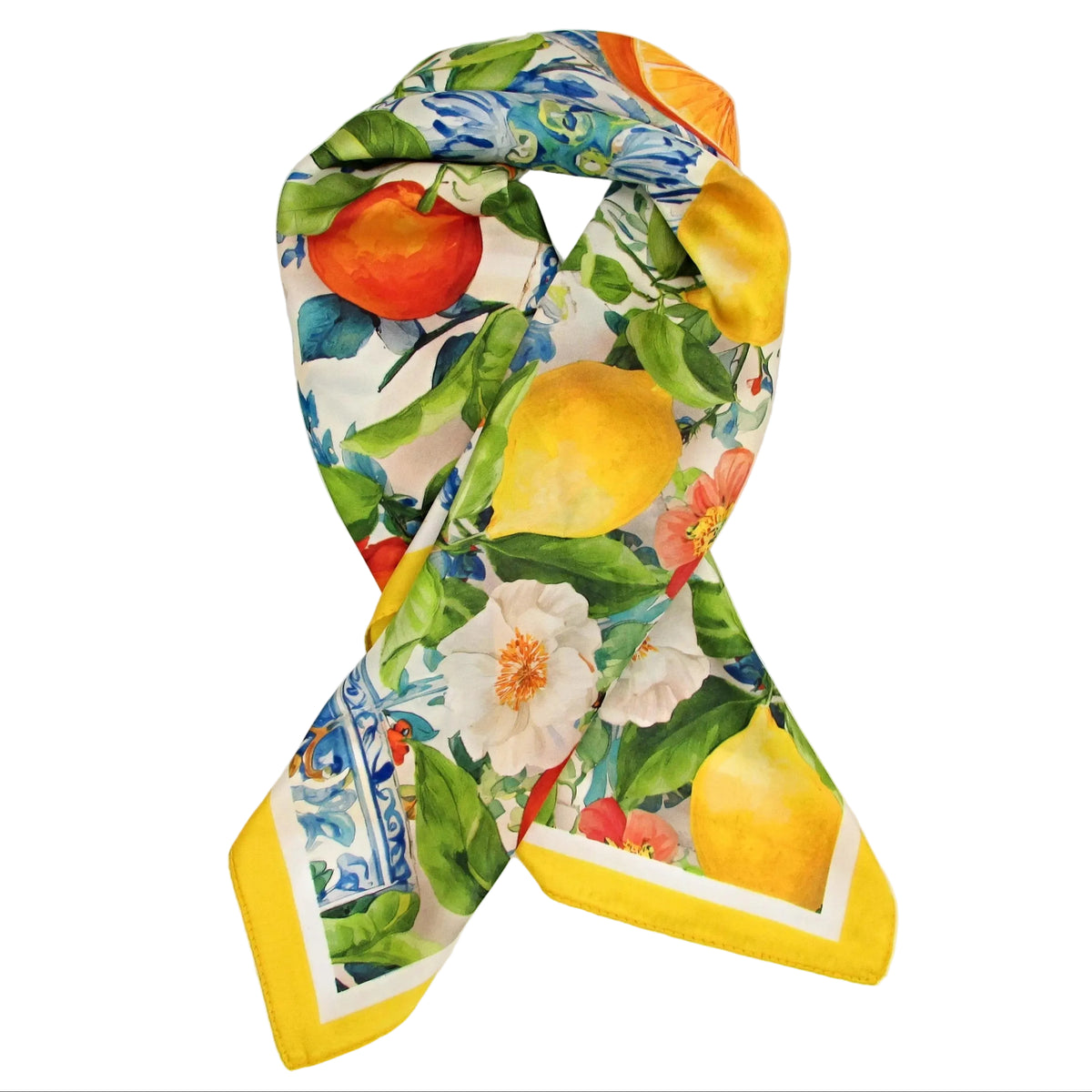 A square silk scarf with a vibrant citrus and floral print, styled in a loop over a white gift box. The print features yellow lemons, red oranges, white flowers, and green leaves on a cream background with blue patterned borders.