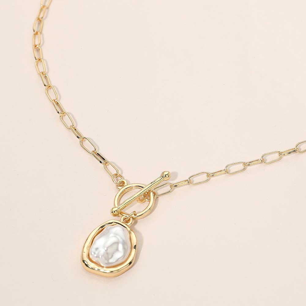 Gold necklace with a teardrop-shaped pearl pendant on a beige background