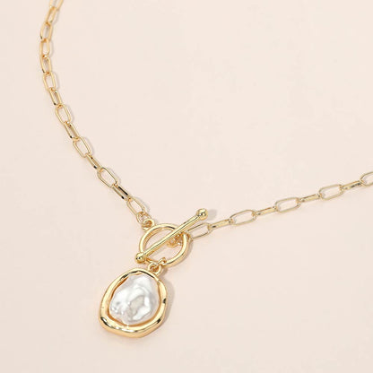 Gold necklace with a teardrop-shaped pearl pendant on a beige background