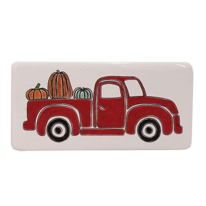 A rectangular ceramic box sign featuring a red truck with a pumpkin load on the back, in a white background.