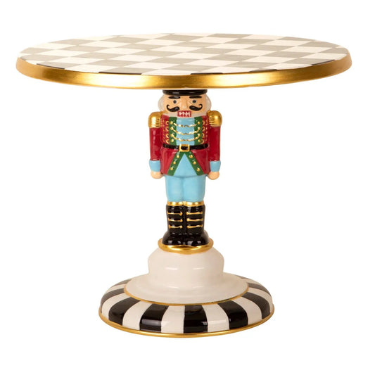 Whimsical nutcracker cake stand with a black and white checkered top, colorful details and gold accents. A festive pedestal server for Christmas treats.