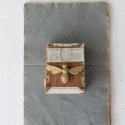 Decorative wall art with a gold bee ornament and vintage-style text on a textured surface