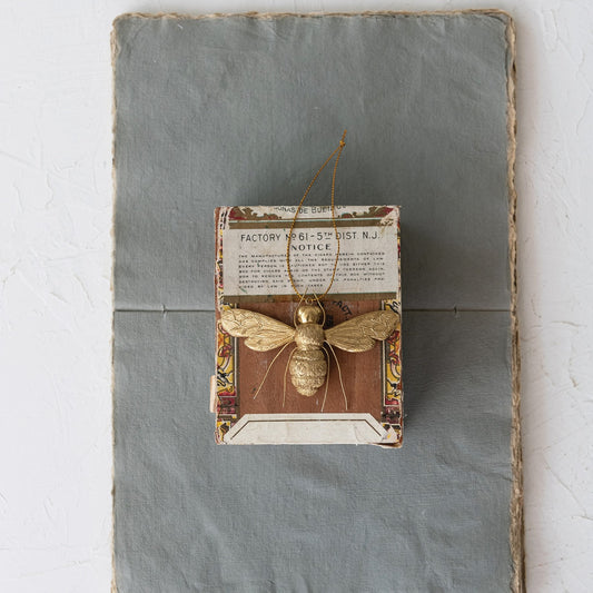 Decorative wall art with a gold bee ornament and vintage-style text on a textured surface