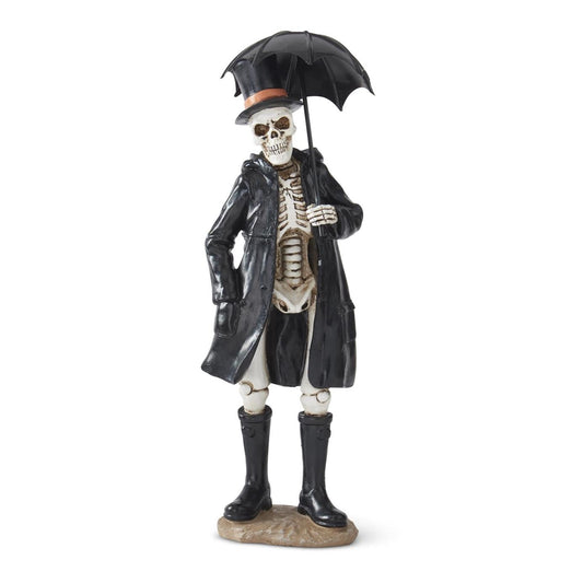 A gothic skeleton figurine dressed in a black trench coat, black rain boots, and a black top hat with an umbrella, standing on a small rock base against a white background.