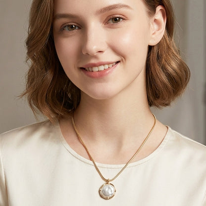 Woman wearing a gold necklace with a pearl pendant against a neutral background