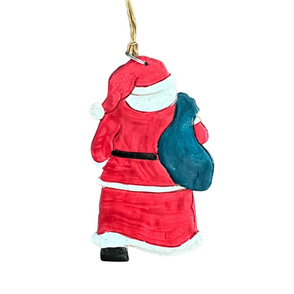 A hand-painted Christmas ornament shaped like Santa Claus carrying a blue sack, resting on a white surface.