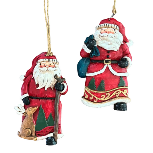 Two hand-painted Christmas ornaments depicting Santa Claus in red and white suits, one holding a walking stick and a reindeer, and the other holding a sack, both hanging from twine on a white background.
