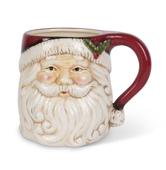 A ceramic Santa Claus mug shaped like his face, with a dark red handle, red hat trim, white beard, and a small green holly accent, shown on a white background.