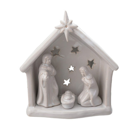 A small white ceramic  nativity scene figurine featuring Mary, Joseph, baby Jesus in a manger, and a star on the roof, set against a plain white background.