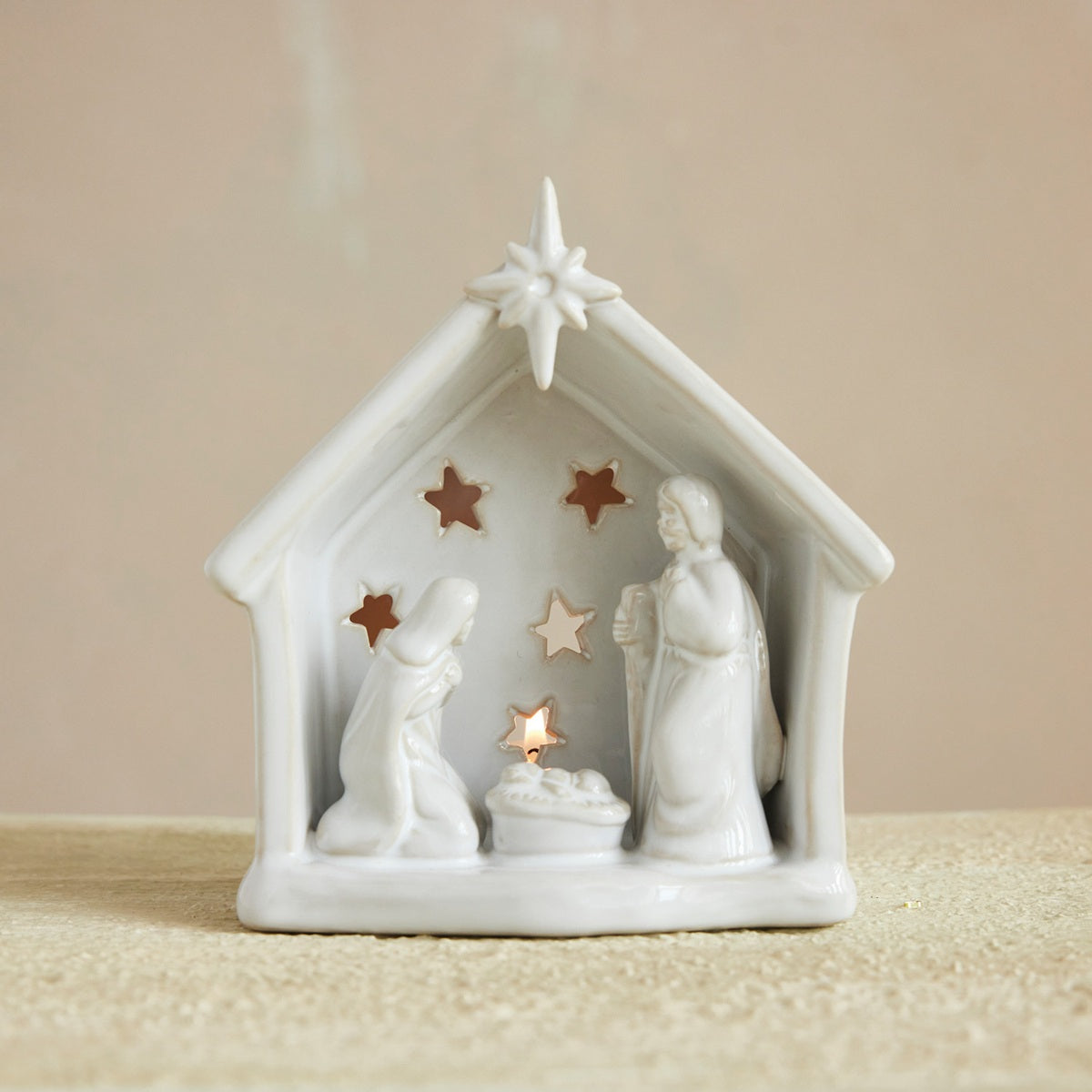 White nativity scene figurine with stars and a candle on a beige background