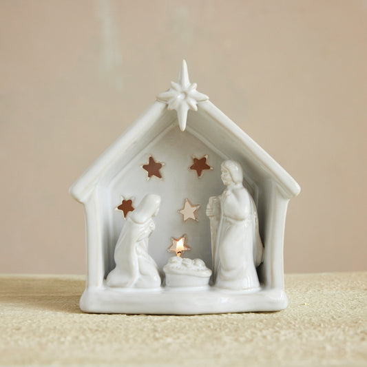 White nativity scene figurine with stars and a candle on a beige background