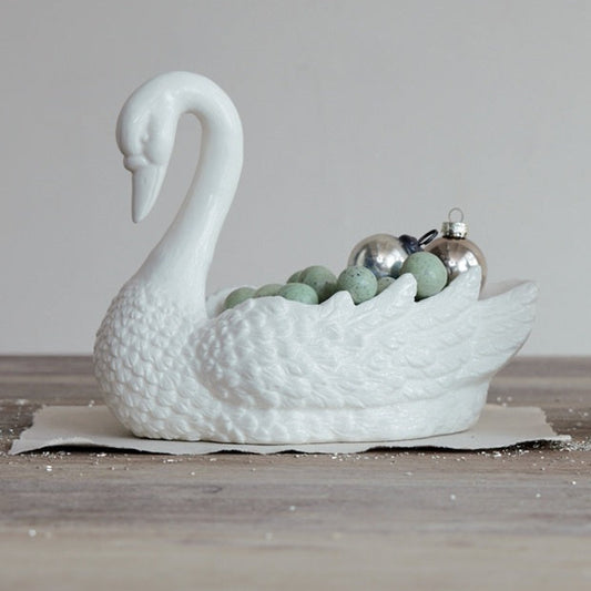 White swan-shaped ceramic bowl on a wooden surface with decorative items inside.