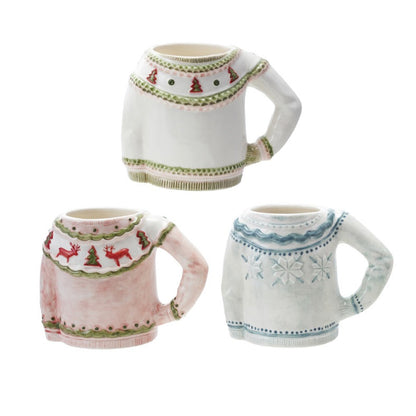 Three ceramic mug-shaped ornaments or figurines with holiday sweater designs, shown on a plain white background. One is white with green trim and red Christmas tree motifs, one is light pink with green trim and red reindeer motifs, and one is white with blue knit-style patterns.