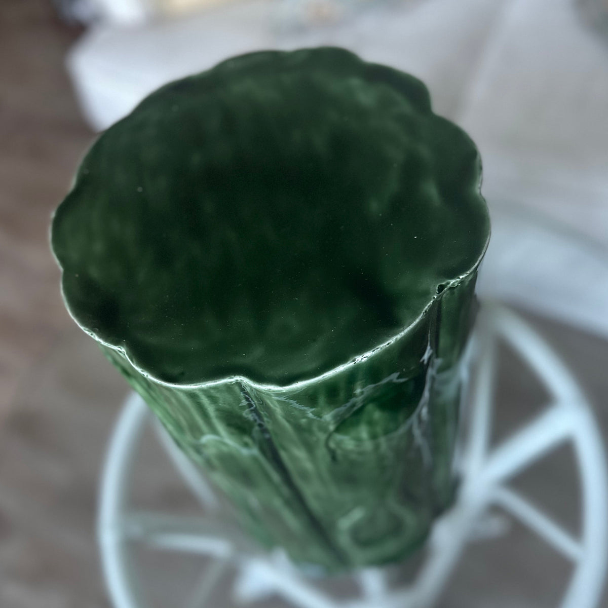 A dark green textured metal stool with a fluted, scalloped rim, shown from a top-down perspective on a white metal stand.