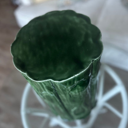 A dark green textured metal stool with a fluted, scalloped rim, shown from a top-down perspective on a white metal stand.