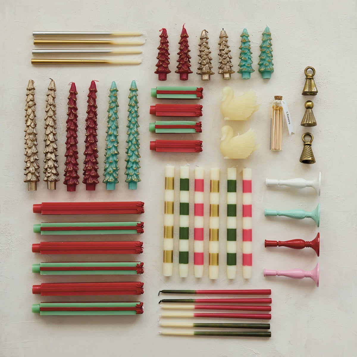 An overhead flat-lay of candles containing various colors and silhouettes in holiday colors like red, green, gold, and white, arranged neatly on a light textured background.