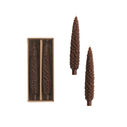 Boxed set of two tall brown pinecone-shaped taper candles shown against a white background.