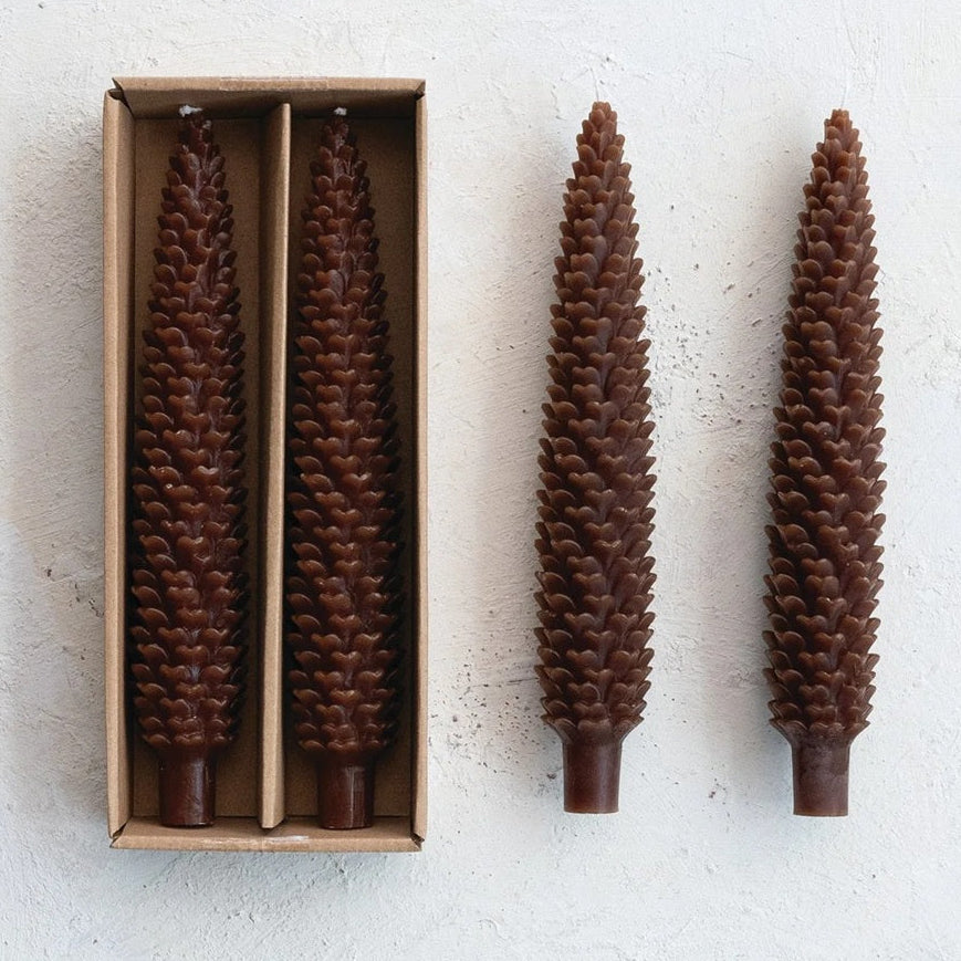 Set of two tall brown pinecone-shaped taper candles displayed beside their kraft box.