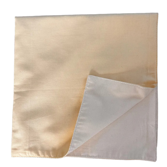 A square yellow and cream-colored fabric napkin with a folded corner revealing the reverse side, placed on a white background. 